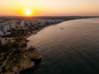Portimo, Algarve, Portekiz 2025.07.01: Portimos ufuk çizgisi, altın kıyı şeridi ve ılık sabah ışığı altında parlayan sakin Atlantik sularının insansız hava aracı görüntüsü 