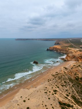 Sagres, Algarve, Portekiz 2025.07.03 Altın uçurumlar, geniş kumlu plaj ve Atlantik Okyanusu dalgalarında sörfçüler.. 