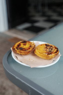 Algarve, Portekiz 2025.07.04 Kafe masasında servis edilen iki geleneksel Pastel de Nata kremalı turtasının yakın çekimi. 