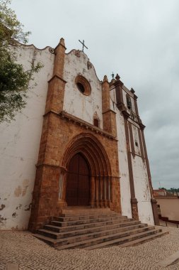 Silves, Algarve, Portekiz 2025.07.04 Silves Katedrali 'nin Gotik kemerli kapısı, taş basamakları ve bulutlu gökyüzünün altındaki tarihi çan kulesi.. 