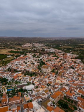 Silves, Algarve, Portekiz 2025.07.04 Silves şehrinin kırmızı çatıları, tarihi şatosu ve bulutlu gökyüzünün altındaki çevresindeki tepeleri gösteren insansız hava aracı.. 