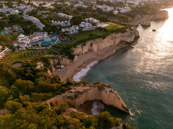 Алгарве, Португалия 20257x1 Вид на восход солнца роскошных курортных садов и бассейнов на золотых скалах, со скрытой бухтой и песчаным пляжем вдоль атлантического побережья. 
