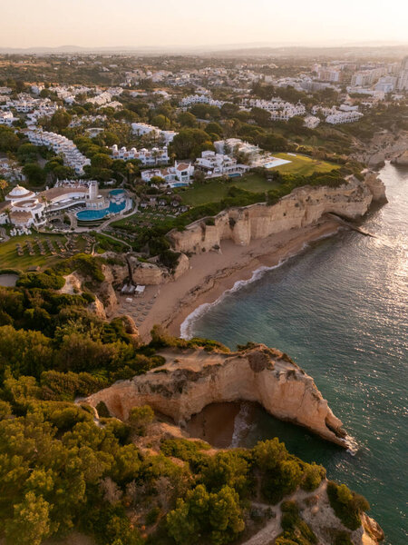 Алгарве, Португалия 20257х1 Беспилотный вид на восход солнца золотых морских скал, скрытые бухты и роскошный курорт с бассейнами и садами, выходящими на атлантическое побережье. 