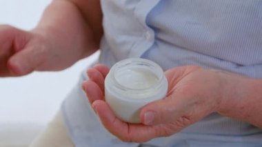 Yaşlı kadınların elleri kavanozdan krem yüz kremi alıp yüzlerine sürerler. Özel güzellik tedavisiyle yaşlanma süreci önlenmesi