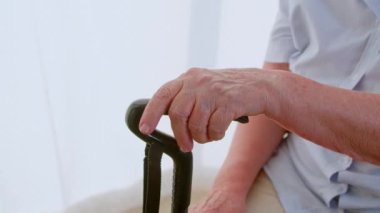 Yaşlı bir kadının elleri ve kireçlenmiş bir baston, yaşlı bakımı. Yaşla ilgili hastalık, huzurevi veya rehabilitasyon kliniği nedeniyle engelli ve bastonlu tanınmayan emekliler.