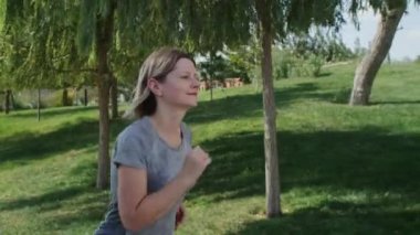 Parkta koşan bir kadına yaklaşmak spor egzersizlerini seven insanlar için harika bir başlangıç. Pozitif duyguları olan kendine güvenen genç bir kadın.