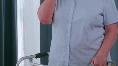 Yürüyen çerçeveli yaşlı kadın yaşlı sağlık hizmetlerini, emekliliği ve sağlık sorunlarını arıyor. Cep telefonundan internet desteği ya da yardım için engelli konuşması yapan mutsuz yaşlı kişi. 