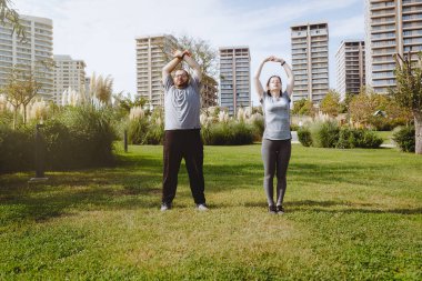 Ekstra kilolu bir adam ve kadın antrenörü koşudan önce parkta ısınıyorlar. Sağlıklı bir yaşam tarzı, sabah antrenmanlarıyla güne başlıyor.