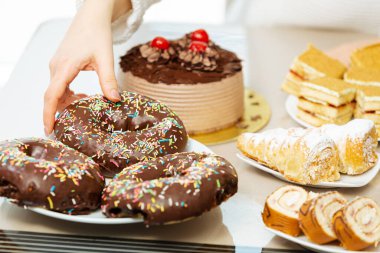 Kadınların eli, tatlı yiyeceklerle çikolatalı donutları alıyor. Yeme problemi ve şeker bağımlılığı yüzünden.