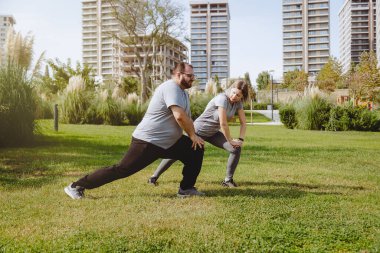 Ekstra kilolu bir adam, antrenörüyle birlikte halka açık parkta çalışıyor. Sabahları karnını gerdiren bir çift kadın ve erkek.