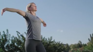 Spor kıyafetli bir kadın parkta antrenmandan sonra rahatlama egzersizi yapıyor. Refah için dinlenme ve meditasyon