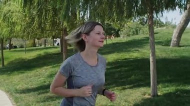 Parkta koşan bir kadına yaklaşmak spor egzersizlerini seven insanlar için harika bir başlangıç. Pozitif duyguları olan kendine güvenen genç bir kadın.