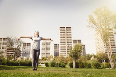 Spor kıyafetli bir kadın parkta antrenmandan sonra rahatlama egzersizi yapıyor. Refah için dinlenme ve meditasyon