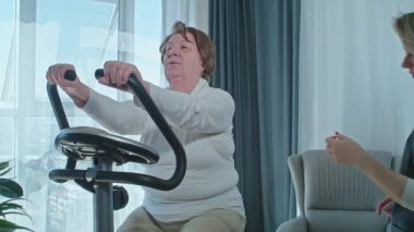 Travmadan sonra sağlığını korumak için bisiklet simülatörü üzerinde egzersiz yapan kıdemli bir kadın.