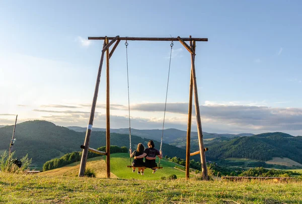 Çiftler yaz günbatımında açık havada ahşap bir salıncakta olmanın keyfini çıkarıyorlar..