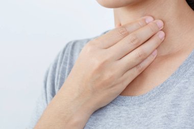  Boğaz ağrısı. Hasta genç kadının iltihaplı boğazını tutarken ellerini kullanarak gri arka plandaki mavi gömlekli hastaya dokunması. Tıbbi ve sağlık hizmetleri konsepti. Acıyı göstermek için kırmızıya odaklan