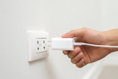 El fişi adaptörünü kapat. Aküyü prizle şarj et ve cep telefonunu duvarda tut. Elektrik güvenliği kavramı.