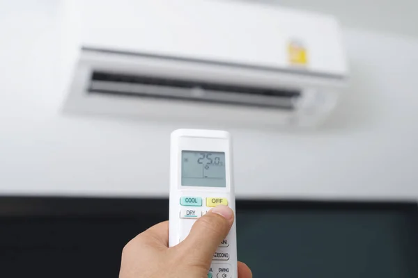 Air conditioner inside the room with close up man hand holding using directed operating remote controller.