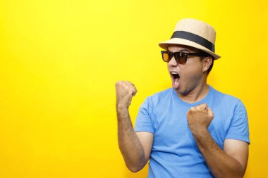 Hippi genç Asyalı adam portresi. Genç mutlu adam. Sıradan, mavi çizgili tişört ve şapka takıyor. Hareketli duygular kolları genişletiyor stüdyo portrelerinde utangaç, sarı arka plan..