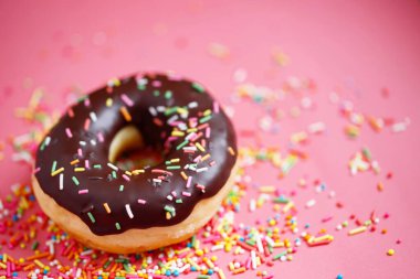 Çeşit çeşit çikolatalı donutlar, üzerine sos serpilmiş renkli çörekler ve çok renkli tatlı çöreklerin karışımı pembe arka planda serpiştirilmiş. en üstteki görünüm