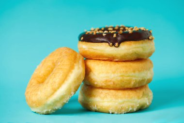 Çikolata kaplı çeşitli çörekler, üzerine sos serpiştirilmiş renkli çörekler ve çok renkli tatlı çöreklerin karışımı mavi arka planda serpilmiş. en üstteki görünüm