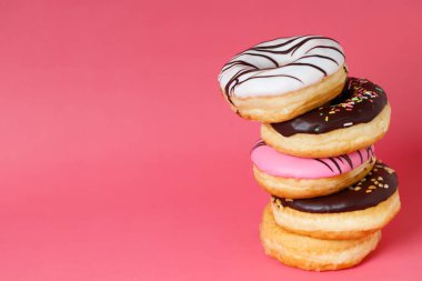 Çeşit çeşit çikolatalı donutlar, üzerine sos serpilmiş renkli çörekler ve çok renkli tatlı çöreklerin karışımı pembe arka planda serpiştirilmiş. en üstteki görünüm