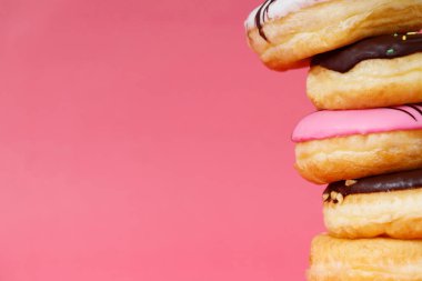 Çeşit çeşit çikolatalı donutlar, üzerine sos serpilmiş renkli çörekler ve çok renkli tatlı çöreklerin karışımı pembe arka planda serpiştirilmiş. en üstteki görünüm