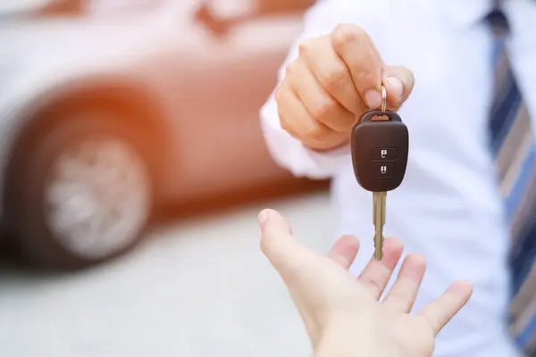 Car key, businessman handing exchange over give to the other man on showroom background. Seller dealer credit Interest payment or purchase by installment car concept.