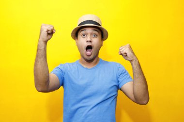 Portrait of cheerful asian man in basic clothing Casual wear red striped T-shirt and wear a hat smiling and show giving thumbs up at camera with showing success. isolated over yellow background.	