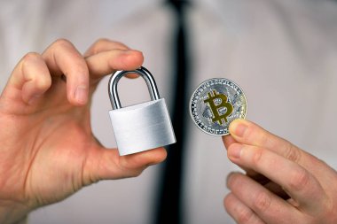 Bir iş adamı elinde gümüş bir asma kilit ve bitcoin 'in fiziksel versiyonunu tutar. Kripto para birimlerinin, yönetmeliklerin, kısıtlamaların veya güvenliğin, korumanın, mahremiyetin yasaklanması.
