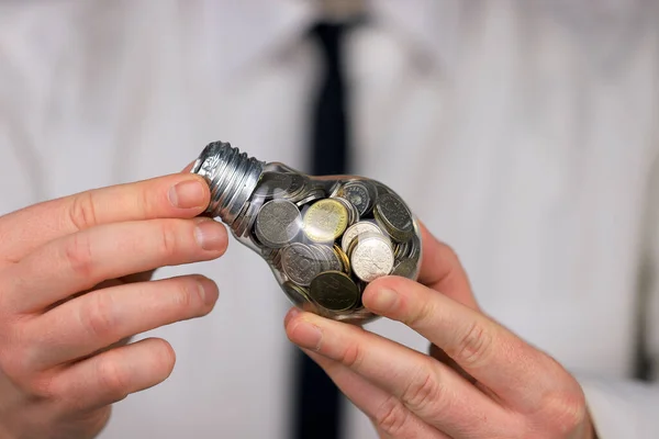 Businessman holding light bulb with coins. Electricity prices, energy saving in the household.