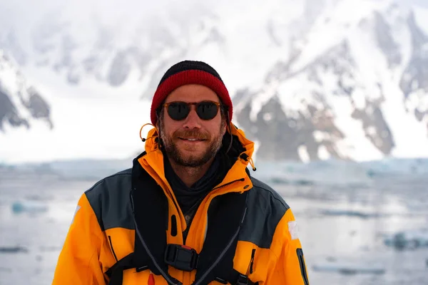 南極の黄色のジャケットを着た若い男性観光客が笑っている 背景に氷山 山の中でバックパックとハイキング — ストック写真