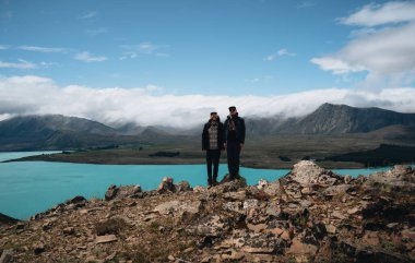 Canterbury Bölgesi, Yeni Zelanda 'da Blue Lake Tekapo' nun önünde iki genç turist duruyor. John Dağı Gözlemevi 'nin küçük tepesinde duran şapkalı genç adamın ön görüntüsü.