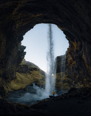Kvernufoss şelale gorge Dağları nın içinde. Turistik cazibe İzlanda. Adam kırmızı ceket ayakta ve düşen su akışını bakar. Doğada güzellik.