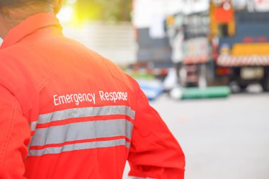 Turuncu renkli acil durum kıyafetli kişi sarı ışıklı tehlikeli bir ürünün yol kazasının yanında duruyor.