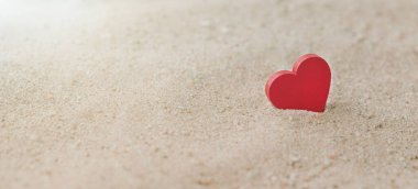 Kumlu bir sahilde, güneş ışığı olan tahta bir kırmızı kalp, Aşk ve Çift kavramı. Sevgililer Günü Konsepti