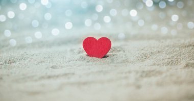 Hafif Bokeh 'li kumlu plajda bir tahta kırmızı kalp, Aşk ve Çift kavramı. Sevgililer Günü Konsepti