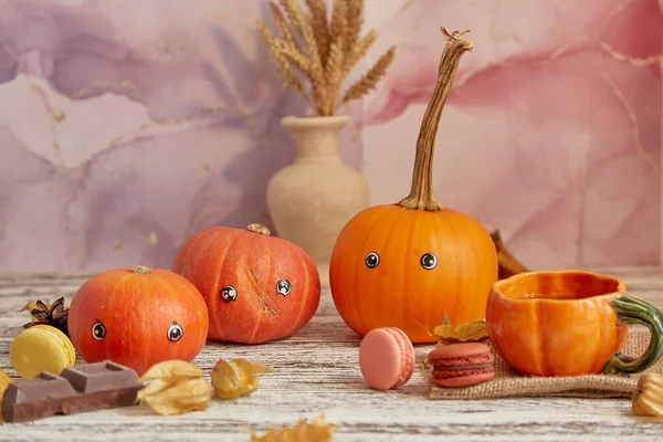 Aesthetic happy halloween pumpkin family with eyes. Cute funny seasonal pumpkins among desserts, cups of tea and winter cherries. Thanksgiving decorations.
