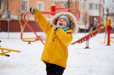 Şehirde karda eğlenen mutlu bir çocuk. Kış eğlencesi dışarıda. Parlak turuncu kışlık ceketli çocuk. Yüksek kalite fotoğraf