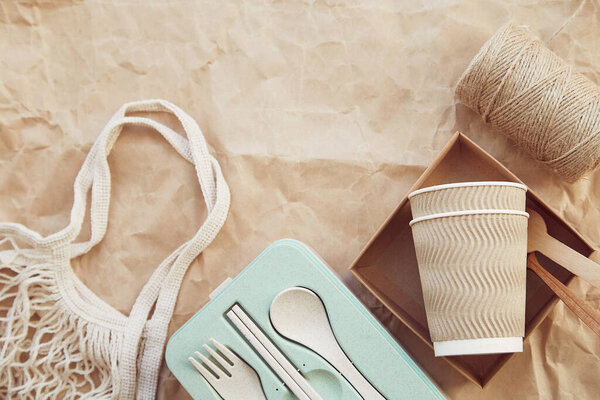 Zero waste, plastic free, sustainable tableware cutlery, cardboard cups made from natural materials and reusable bag on crumpled paper