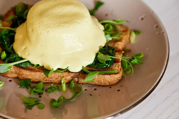 stock image Close up of vegan alternative eggs benedict dish with wholegrain bread, creamy plant-based hollandaise sauce, tofu, young onion, greens, pea sprouts