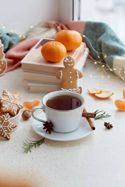 Cozy home food - aesthetics coffee, gingerbread cookies, tangerines near books. Christmas holidays mood in snowy day outside.