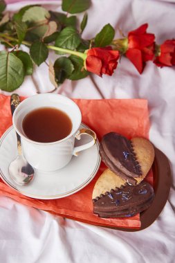 St Valentines breakfast in bed among red traditional roses - vegan heart shaped cookies and coffee cup on the sheets. Aesthetics, romantic lagom holiday background.