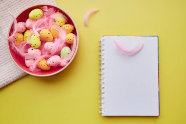 Not defteri maketi. Renkli yumurta ve pembe tüylü pembe kase. Mutlu Paskalyalar. Sarı arkaplanda kartpostal modeli