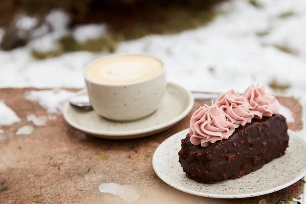 Vegan brownie cake with cup of cappuccino outside. Coffee with dessert. Winter aesthetics.
