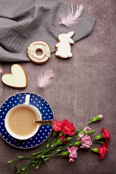 Easter minimalistic coffee time. Glazed cookies, coffee cup, feathers, aster flowers flat. lay. Spring stylish background.