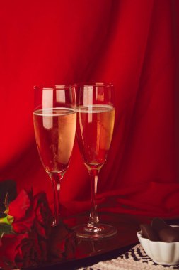 Glasess of champagne in front of red bacground. Romantic seasonal Valentine holiday with roses, candies. Vertical photo.
