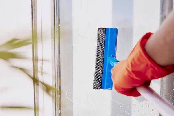 stock image Man is washing windows close up. Disinfection during quarantine due to coronavirus. Household chores. Spring cleaning concept. Dimensional plant, layers, blurred foreground .