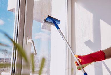 Lastik parlayan adam güneşli bir günde camları yıkıyor. Bahar temizliği, ev işleri konsepti. Boyutsal bitki, bulanık önplan.