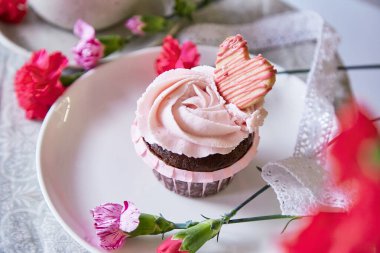 Floral cupcake among flowers decoration. Escapism concept of dreamy french desserts. Spring food background.